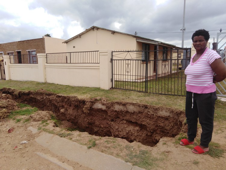 Photo of Eunice Dama pointing out the large trench in front of her yard