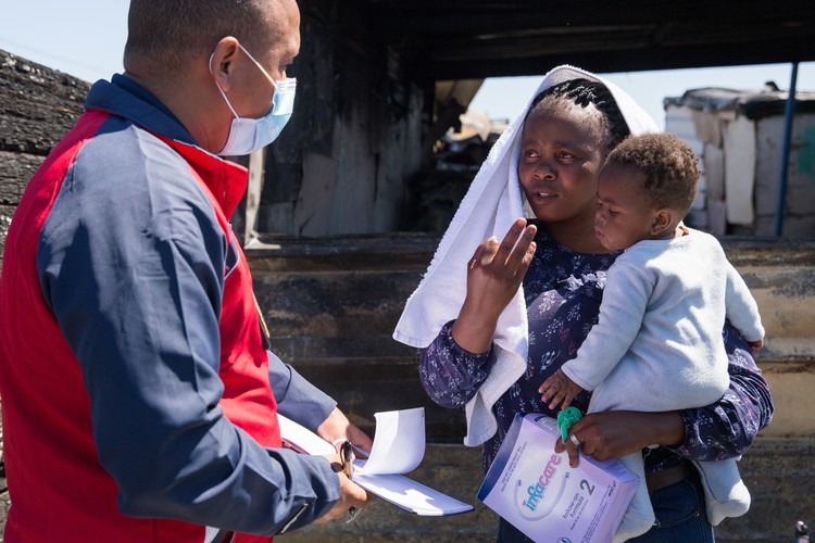 Lona Myeko holds her six-month-old son Melokuhle while speaking to Ashwin Maxim of the City of Cape Town’s disaster risk management centre on Thursday. Photo: Ashraf Hendricks