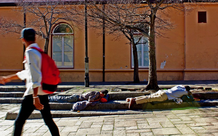 Photo of two people sleeping on the pavement and a passerby