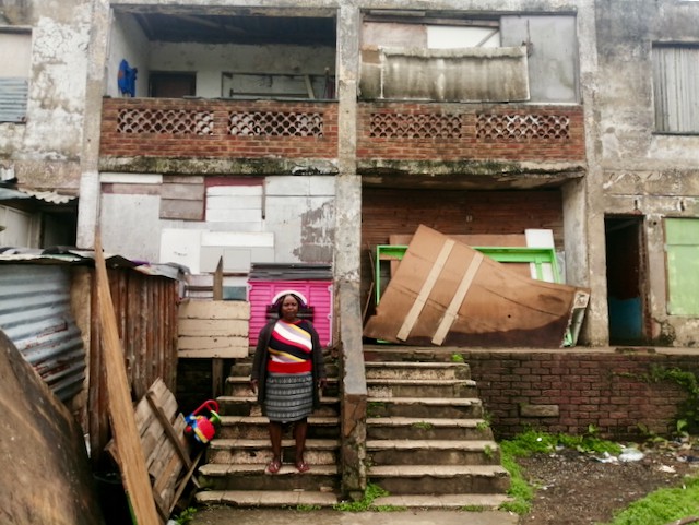 Photo of a woman in front of a dilapidated building