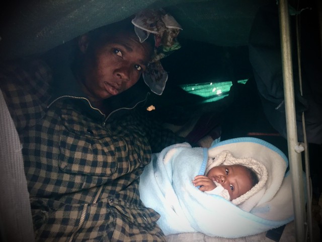 Photo of a woman with her baby under a tarpaulin 