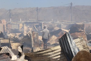 Photo of man standing in the middle of burnt shacks