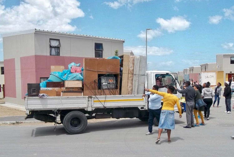 Photo of a truck loaded with furniture being stopped by a crowd
