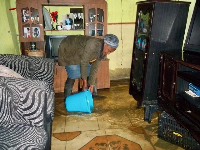 Photo of a woman bailing water in her home with a bucket