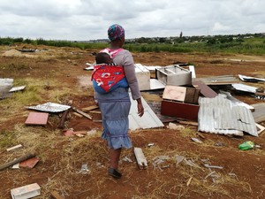Photo of demolished shacks with woman and child looking on