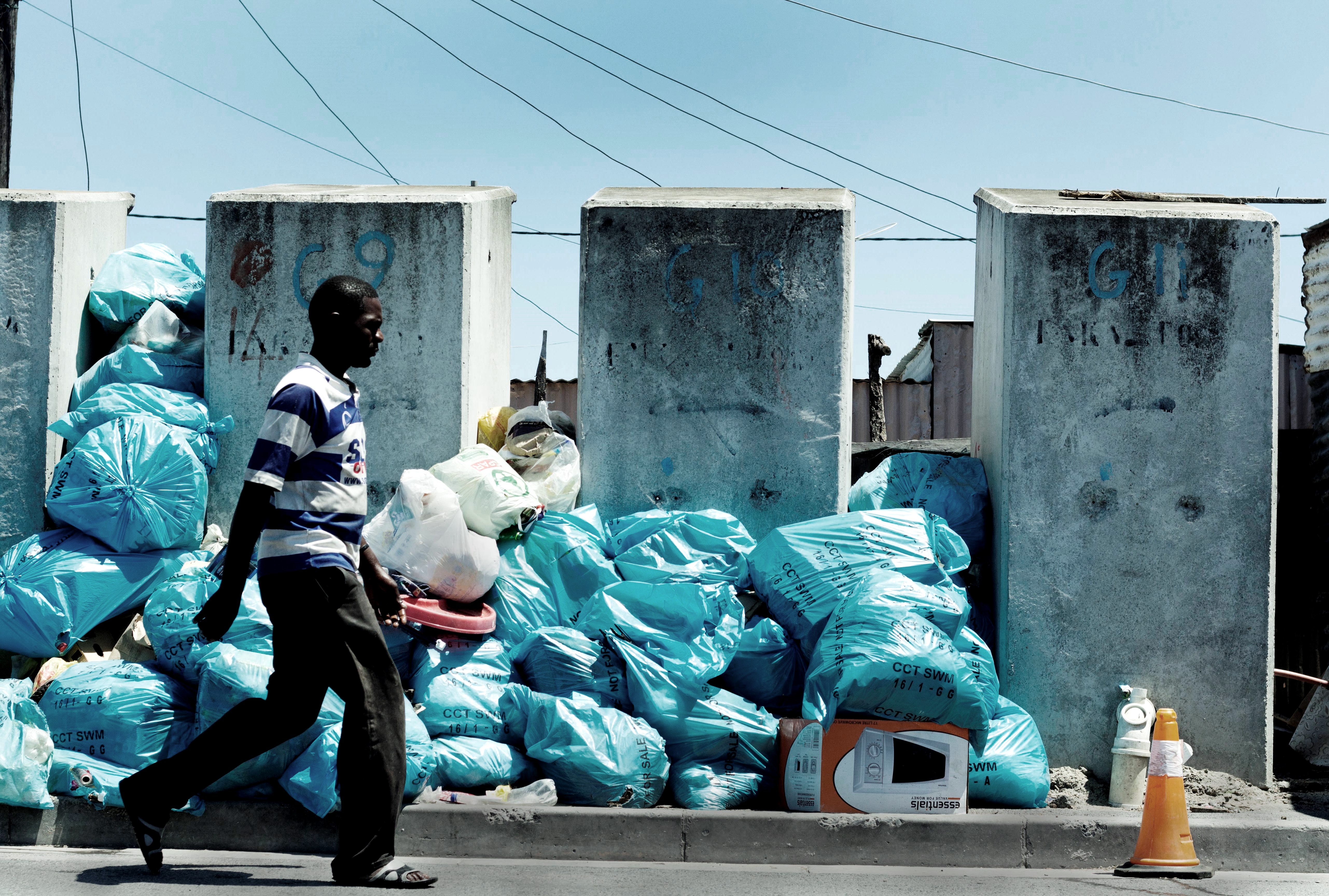 Photo of man walking in street with rubbish piled high