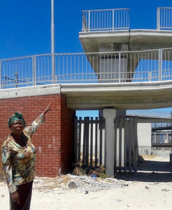 Photo of a woman standing pointing to a missing railing on a bridge